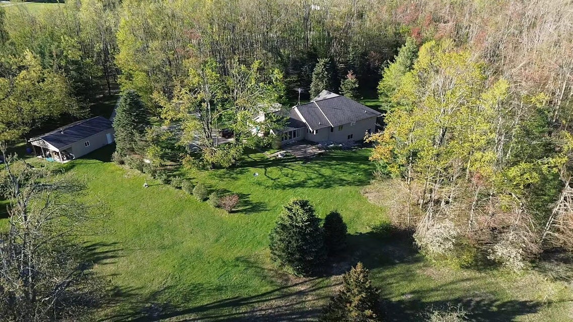 Aerial view of the home surrounded by woods and lawn